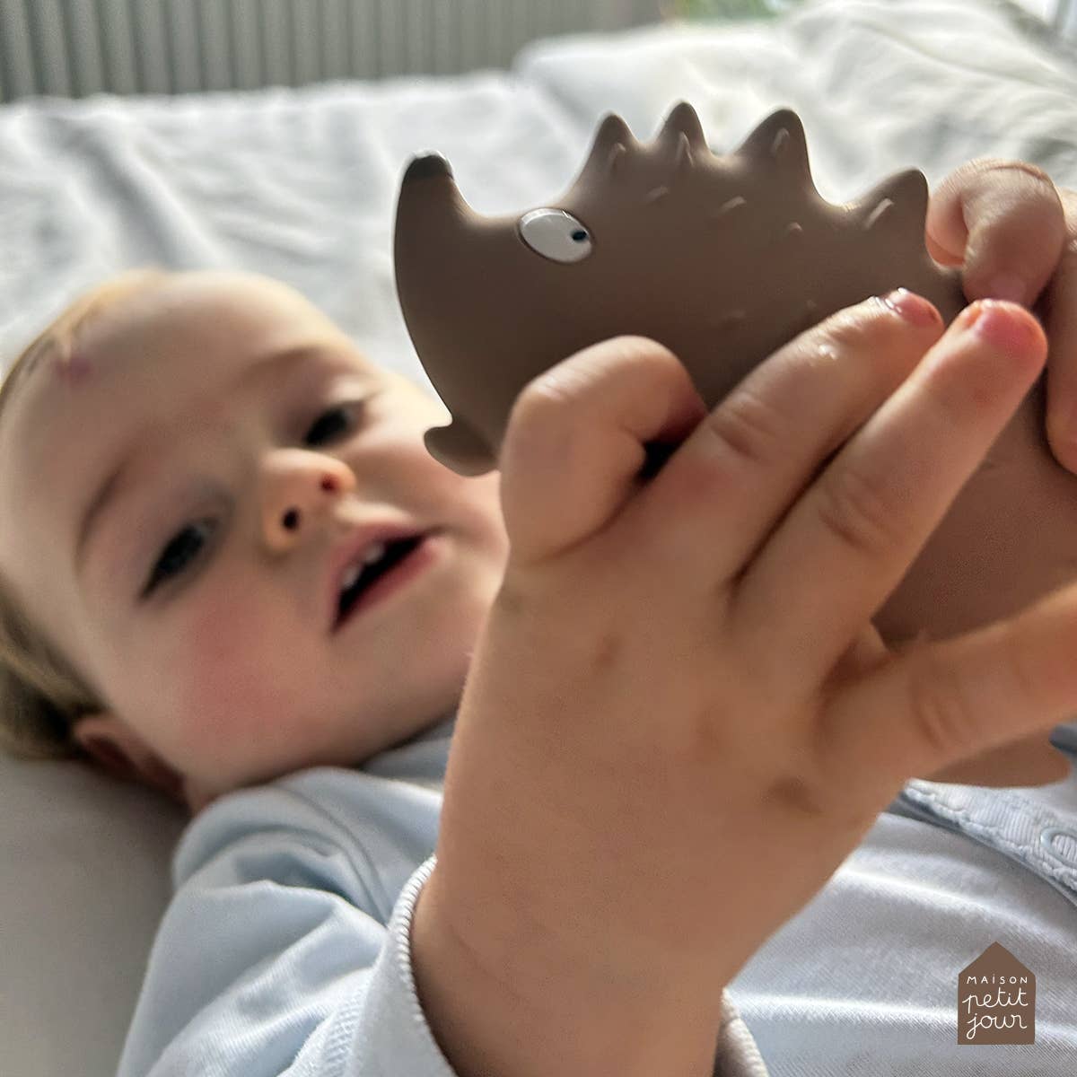 Baby holding hedgehog teether laying in a crib.