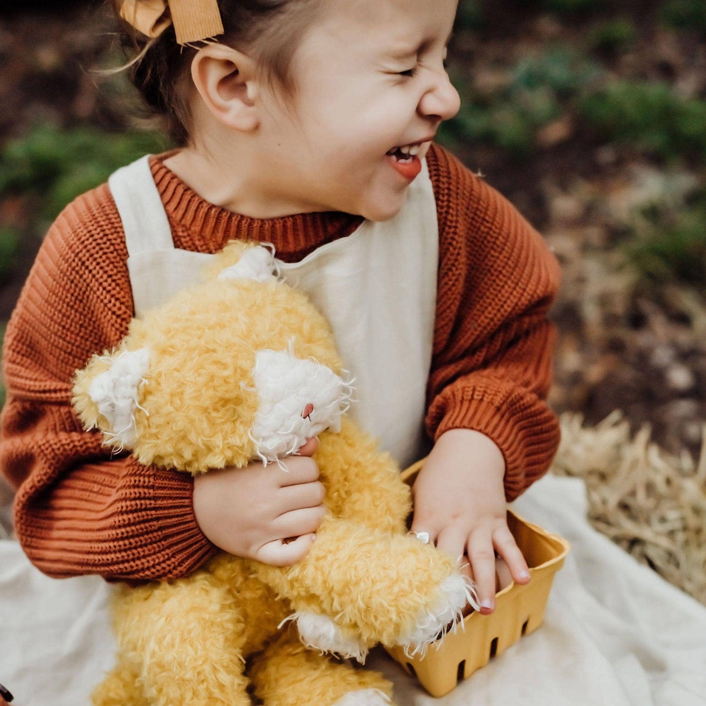 Child holding a yellow teddy bear outdoors