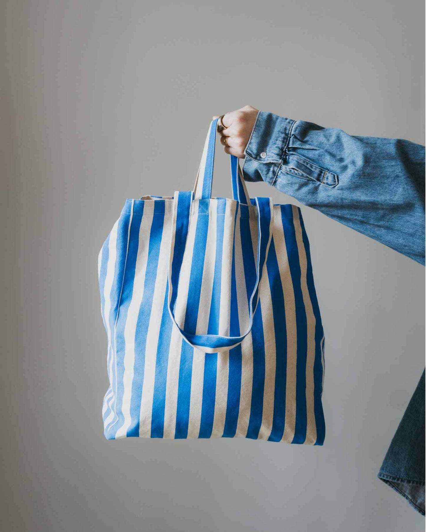 Person holding a blue and white striped tote bag against a plain background