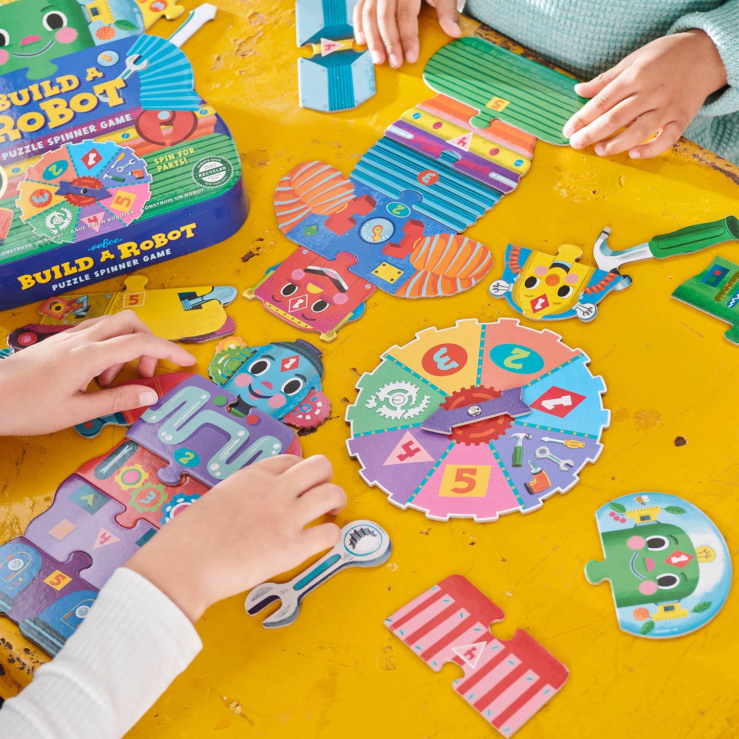 Children playing with a colorful puzzle spinner game on a yellow table.