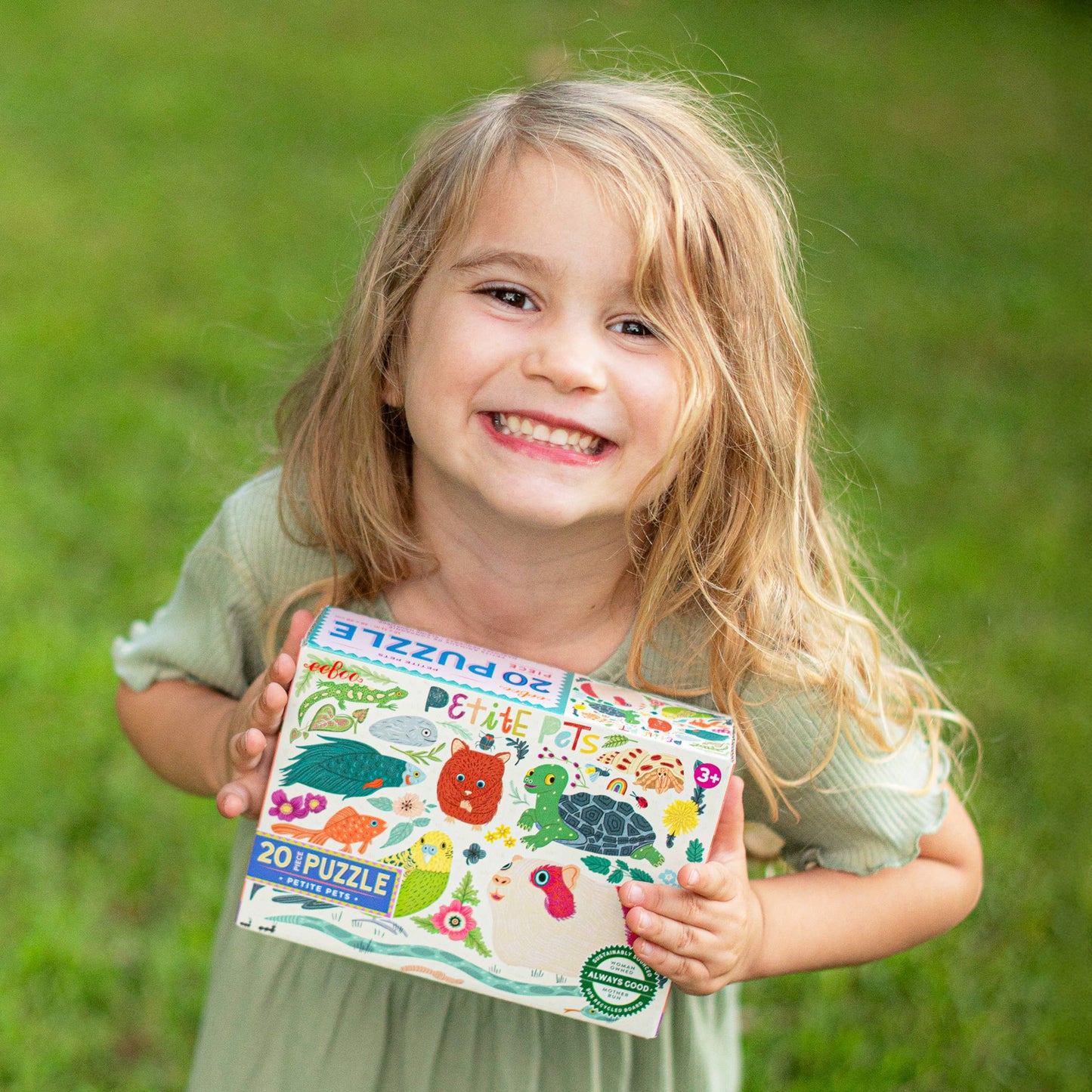 Child holding a children's puzzle book outdoors on grass