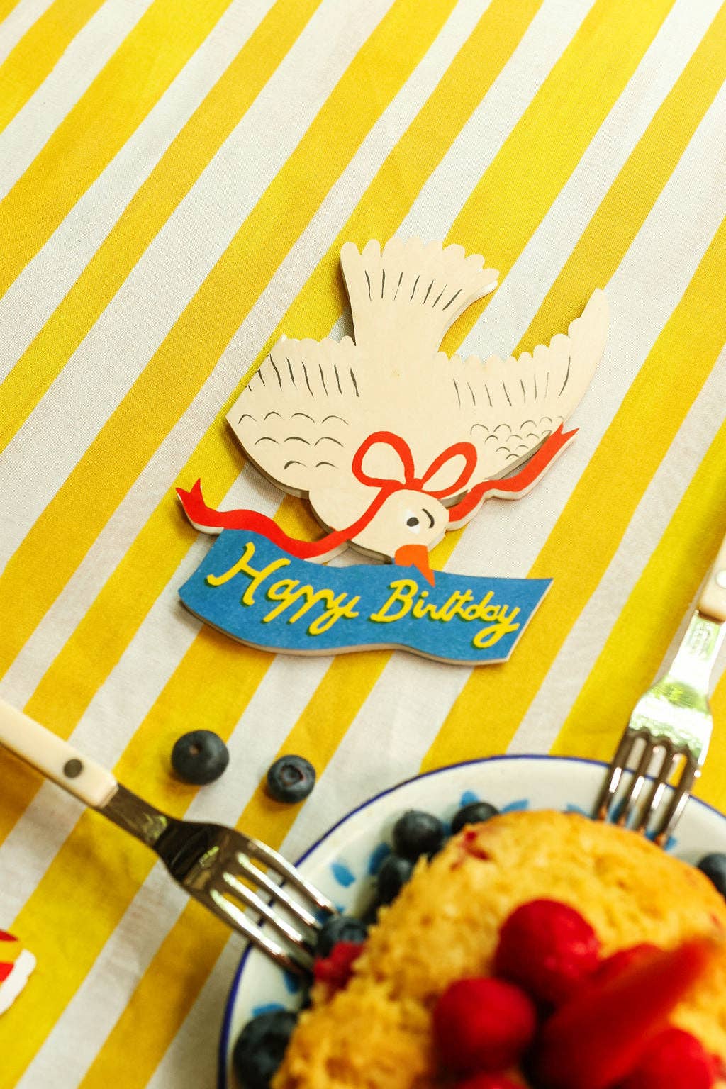 Happy Birthday card with a dove design on a yellow and white striped background with a plate of food and forks nearby.