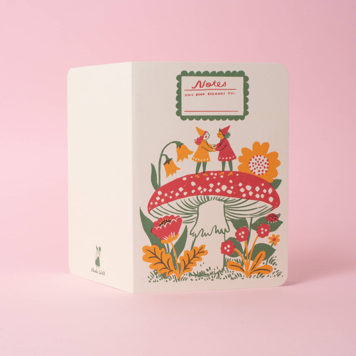 A softcover saddle-stitch notebook with vibrant wraparound cover featuring two gnomes on top of a red toadstool, on a pink background