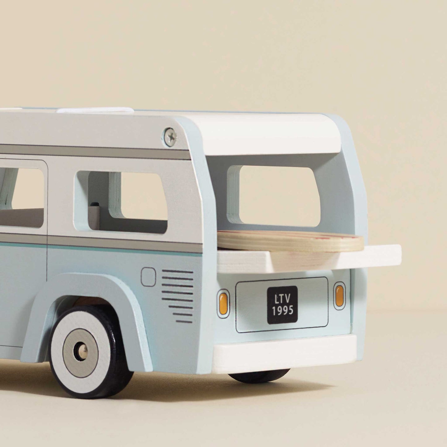 A wooden holiday camper van toy in pastel mint green and cream colors, with a surfboard attached to the side and a removable roof with back open and surf board sticking out of the back