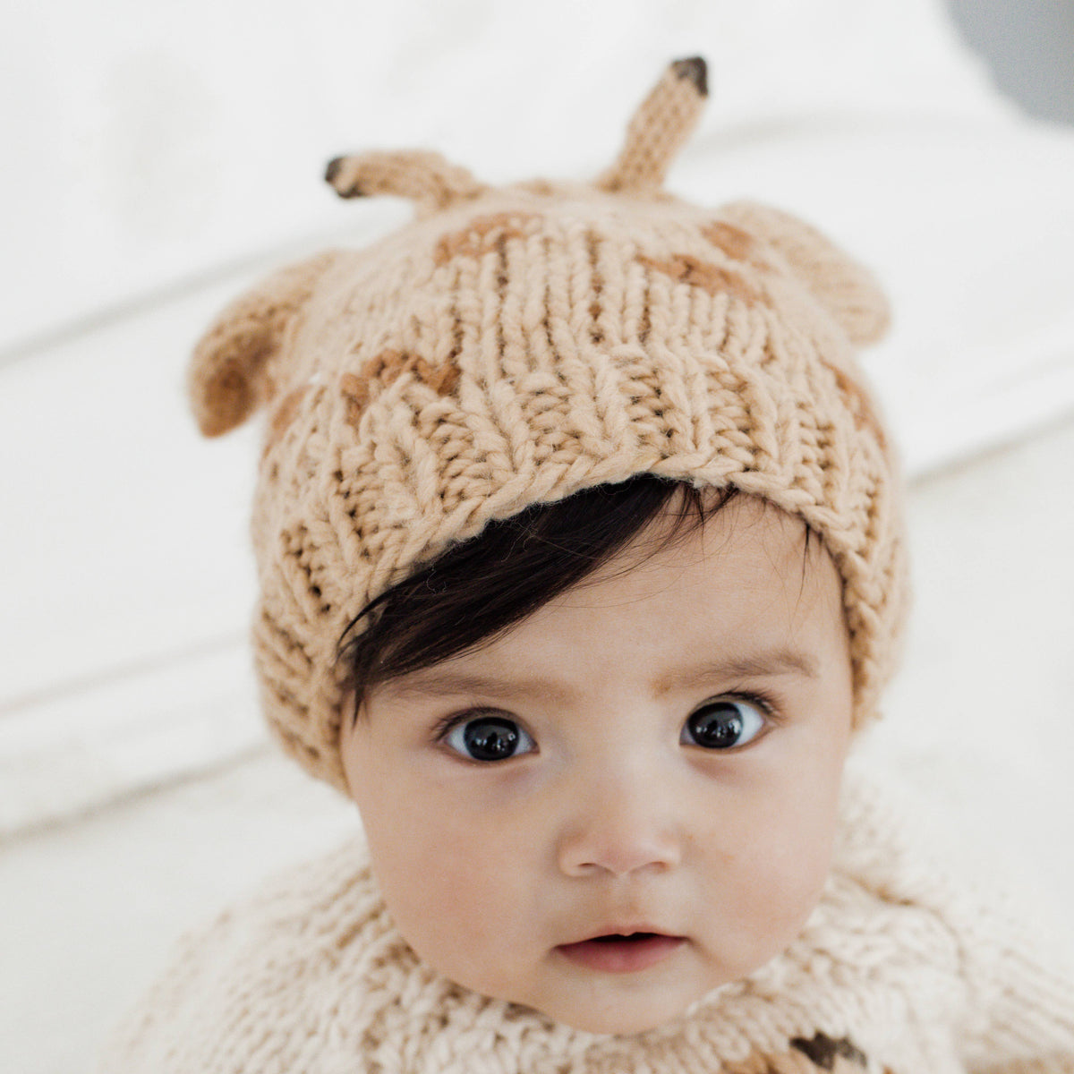 Baby wearing knitted giraffe hat in front of a blurred white background
