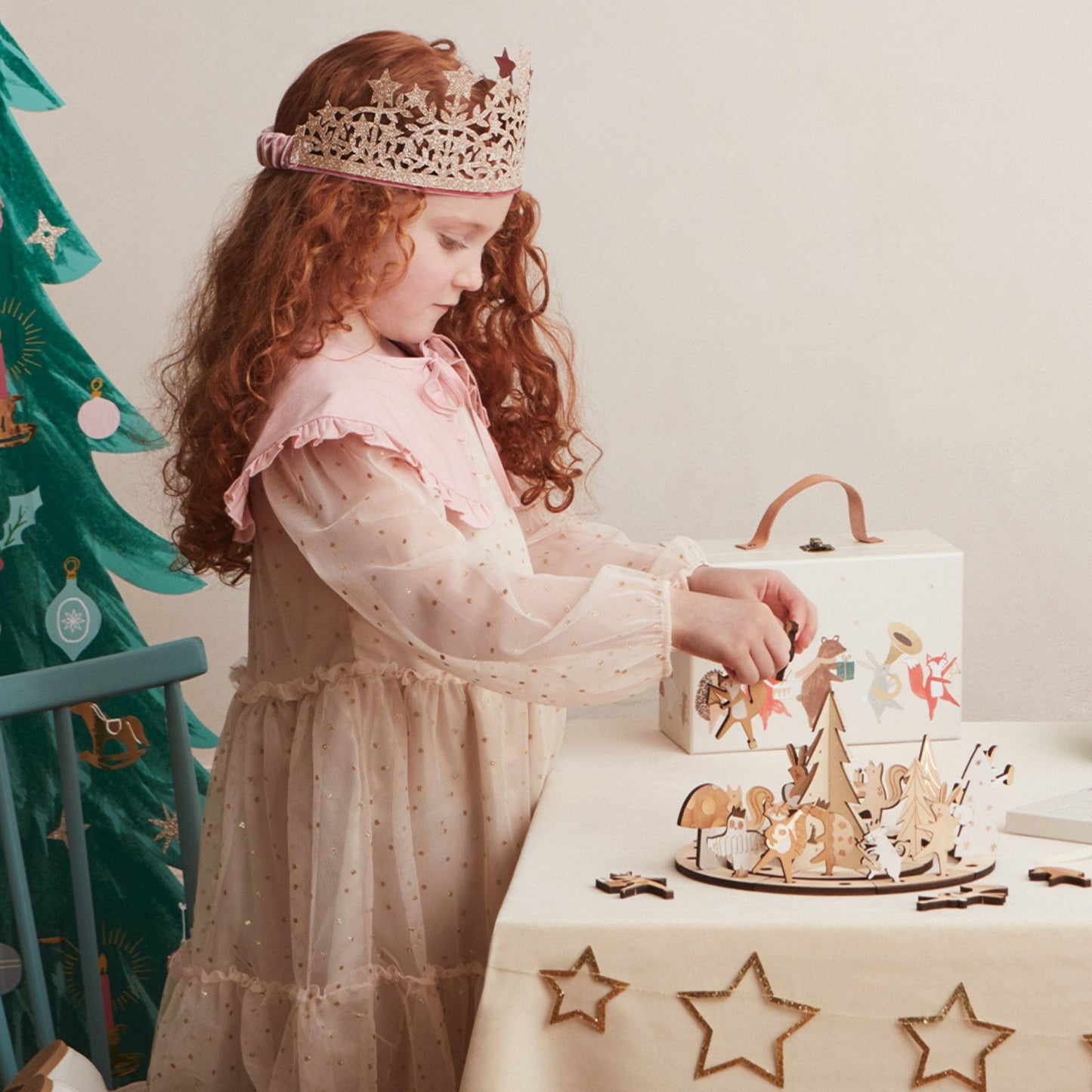 Young girl in a princess dress and tiara playing with a toy set on a table.
