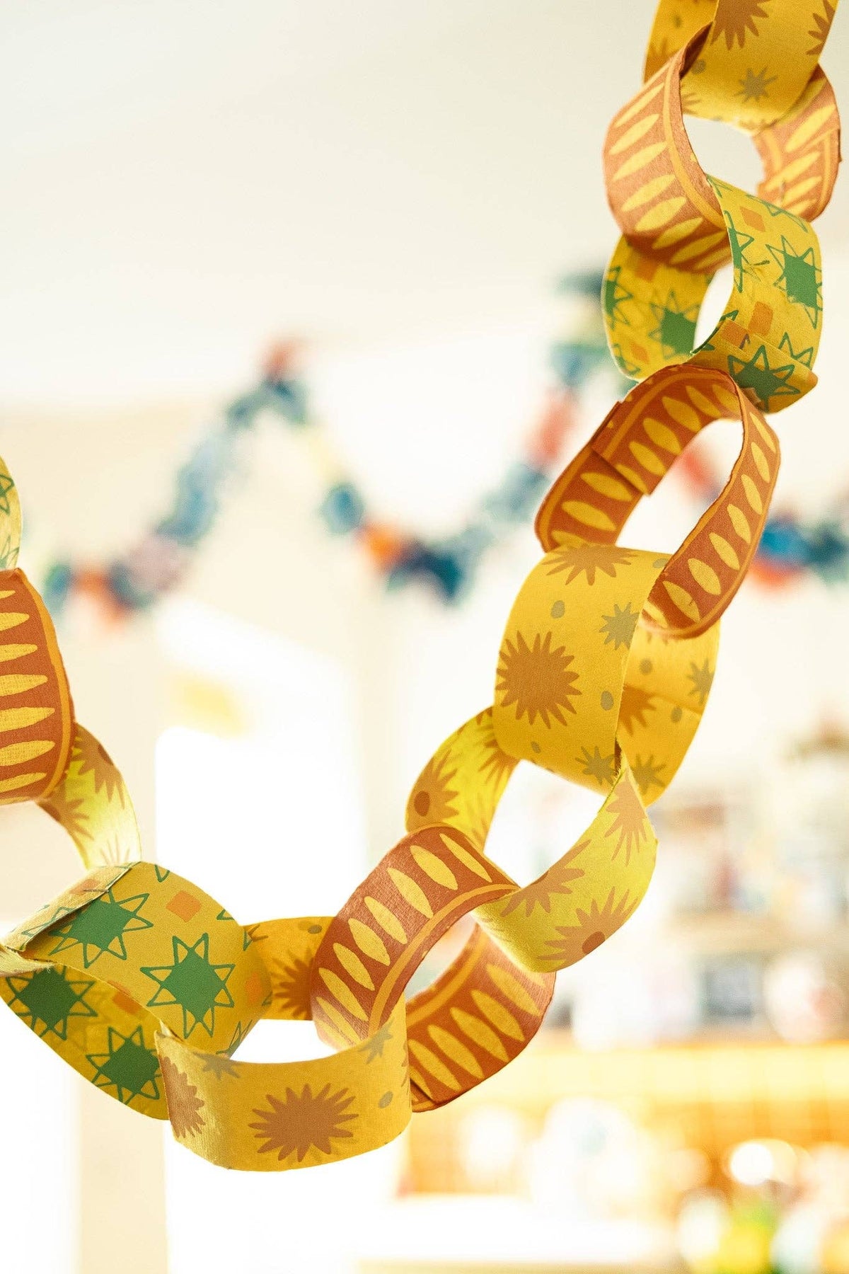 Close-up of hanging yellow, green and orange paper chain links with sunburst and stripe patterns.