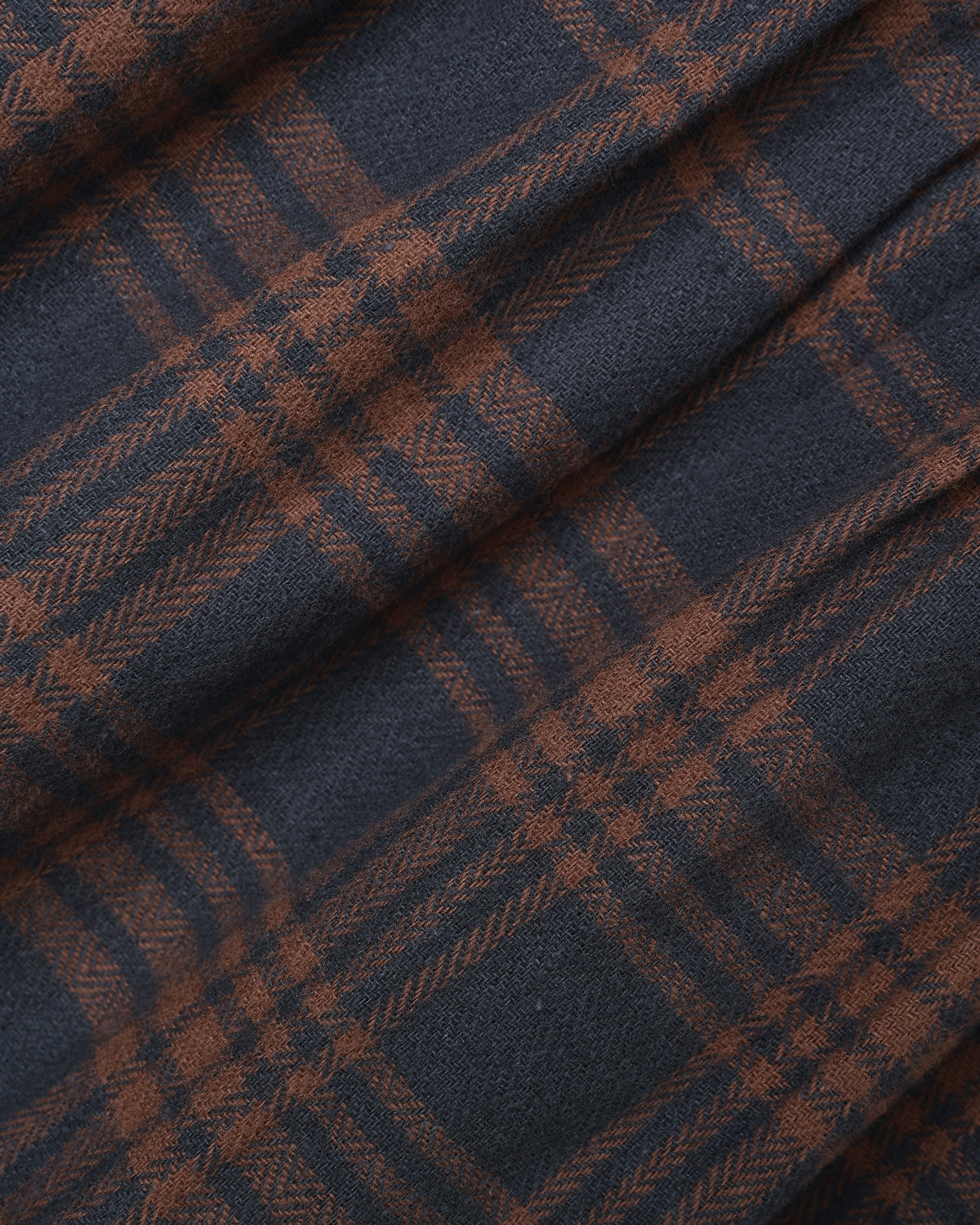 A close-up of a plaid fabric with a dark navy blue base and rust-brown intersecting stripes, showing a soft woven texture with elegant folds.