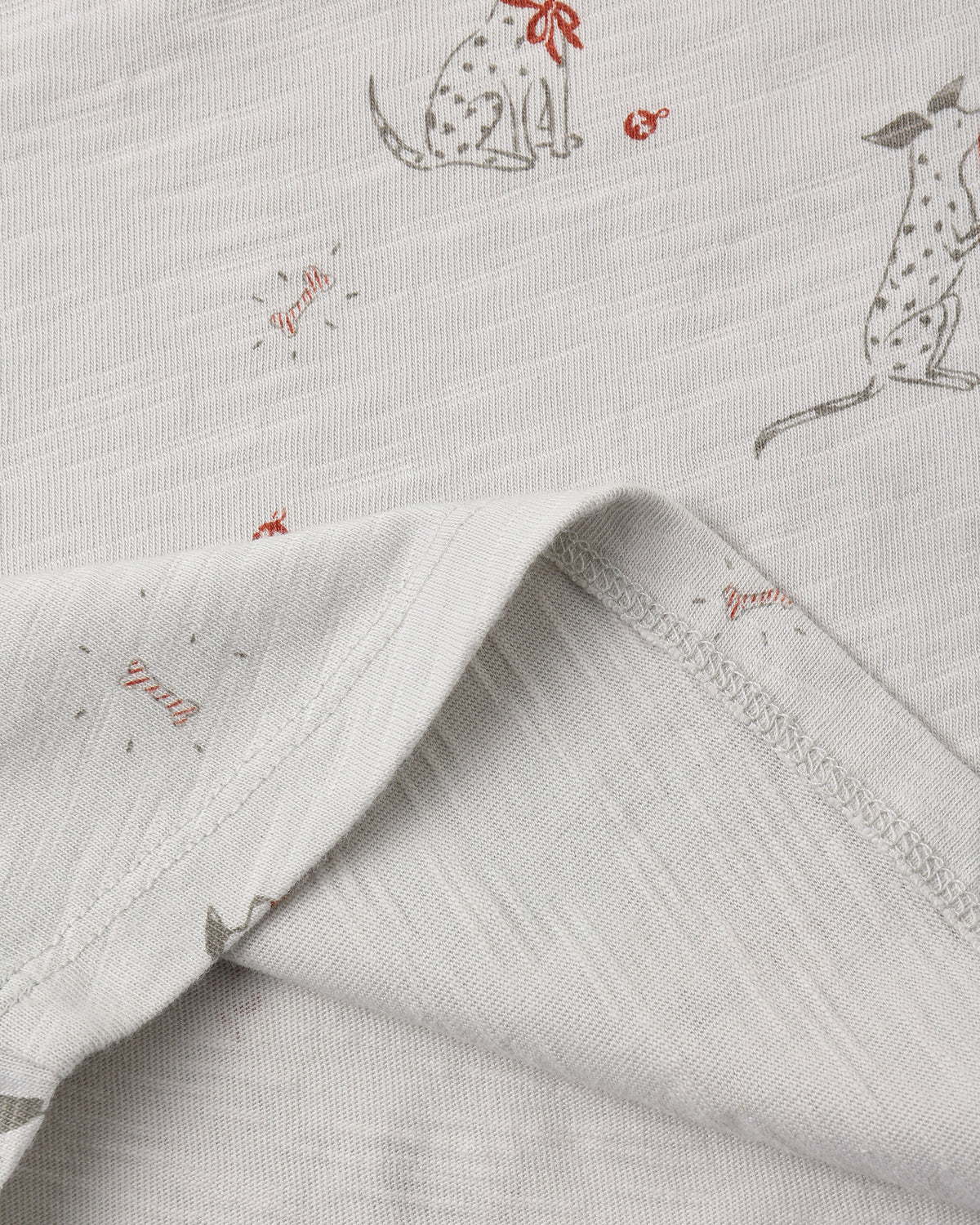 Close-up of a light gray cotton fabric with a printed pattern of dalmations, with a folded corner showing the texture and stitching.