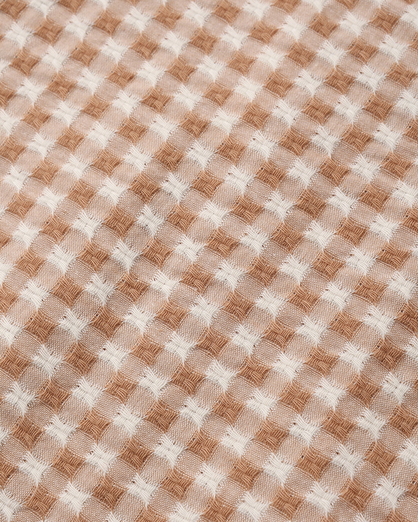 A close-up of a woven fabric with a tan and off-white gingham pattern.
