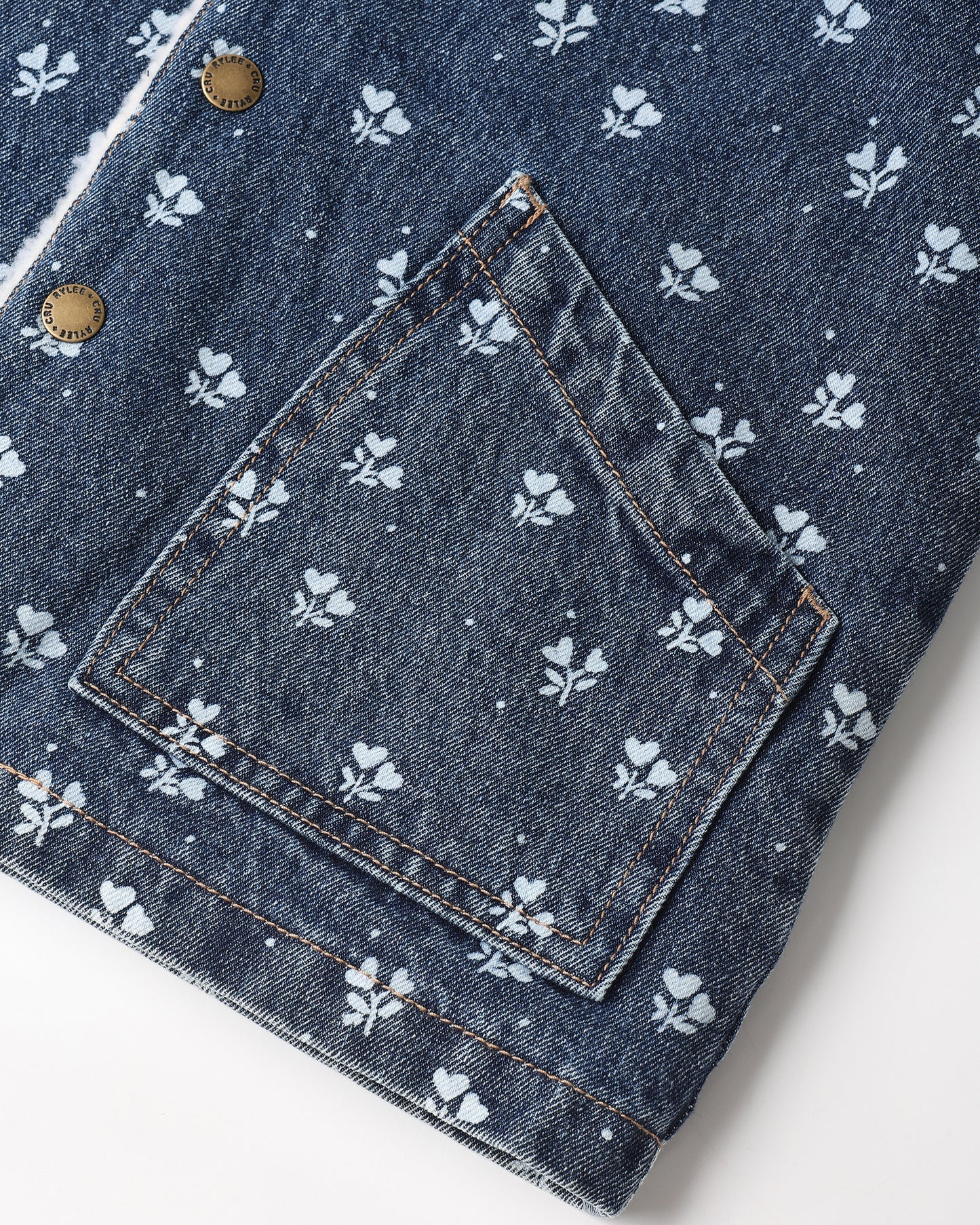 Close-up of a dark blue denim jacket featuring a white floral and dot pattern, a large patch pocket, and brass snap buttons.