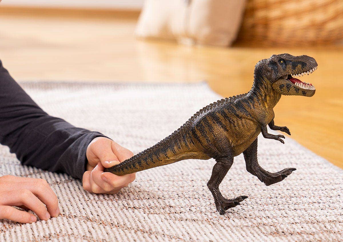 Photo of a child's hands playing with a toy tarbosaurus on a beige rug