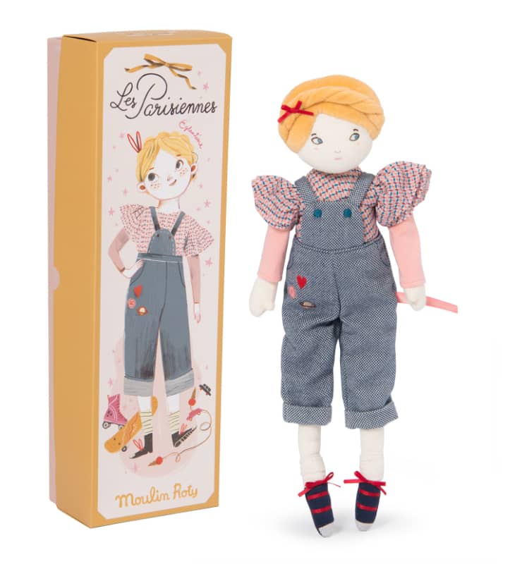 A plush doll named Eglantine the Parisienne from the 'Parisennes' collection, featuring a bicycle, embroidered dungare, lace-up pumps, and a braided hairdo. The doll is displayed next to its packaging box with a design illustration.