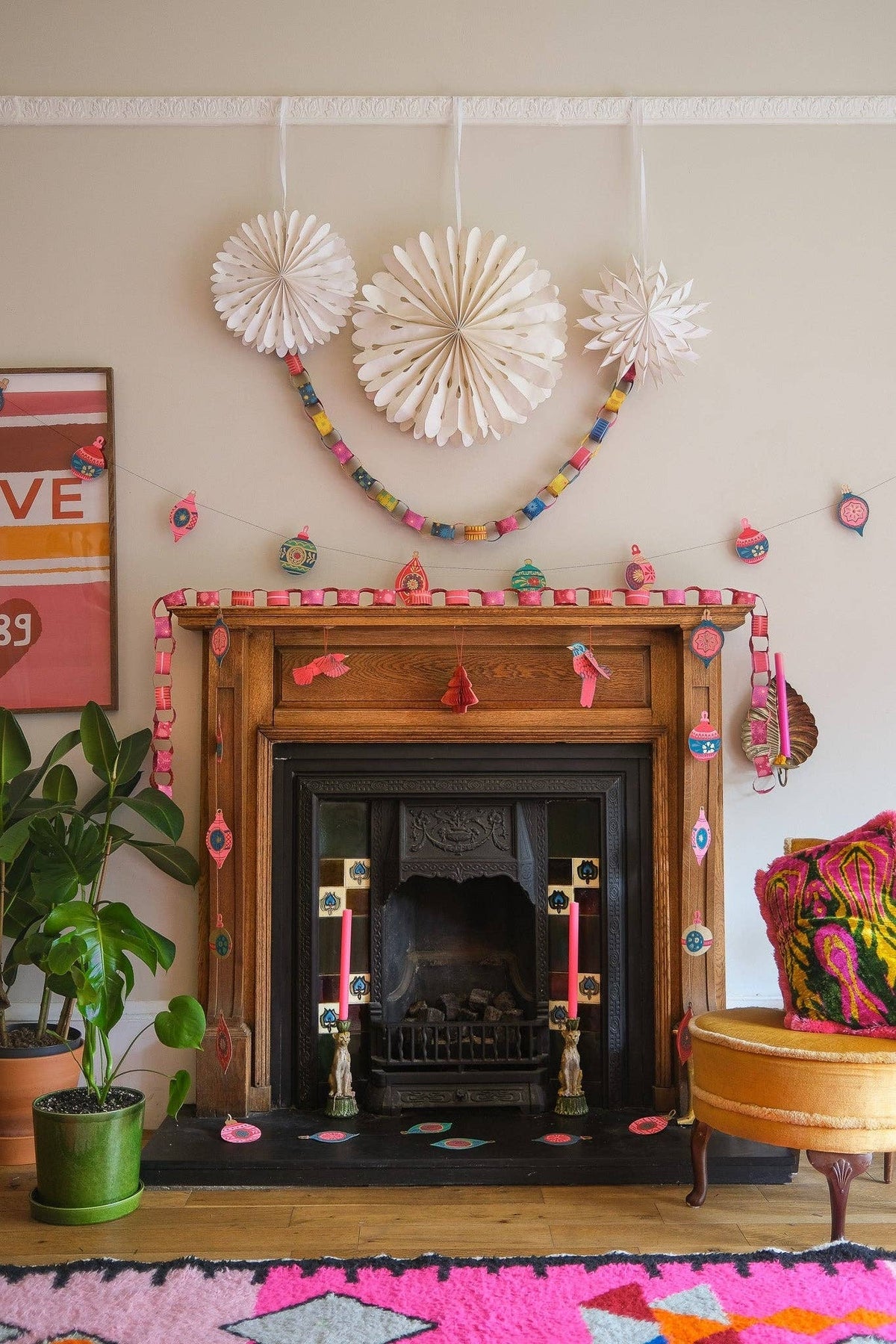 Wooden fireplace decorated with pink paper chains, colorful paper garlands and white rosettes.