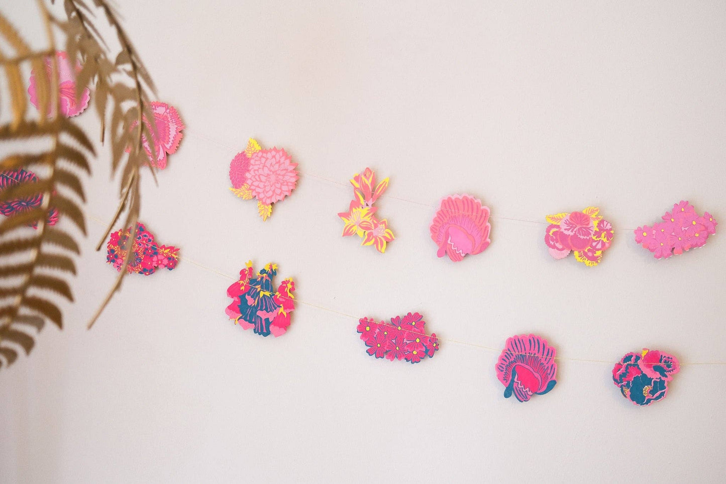 Colorful embroidered garlands on a white background with a leafy branch on the left.