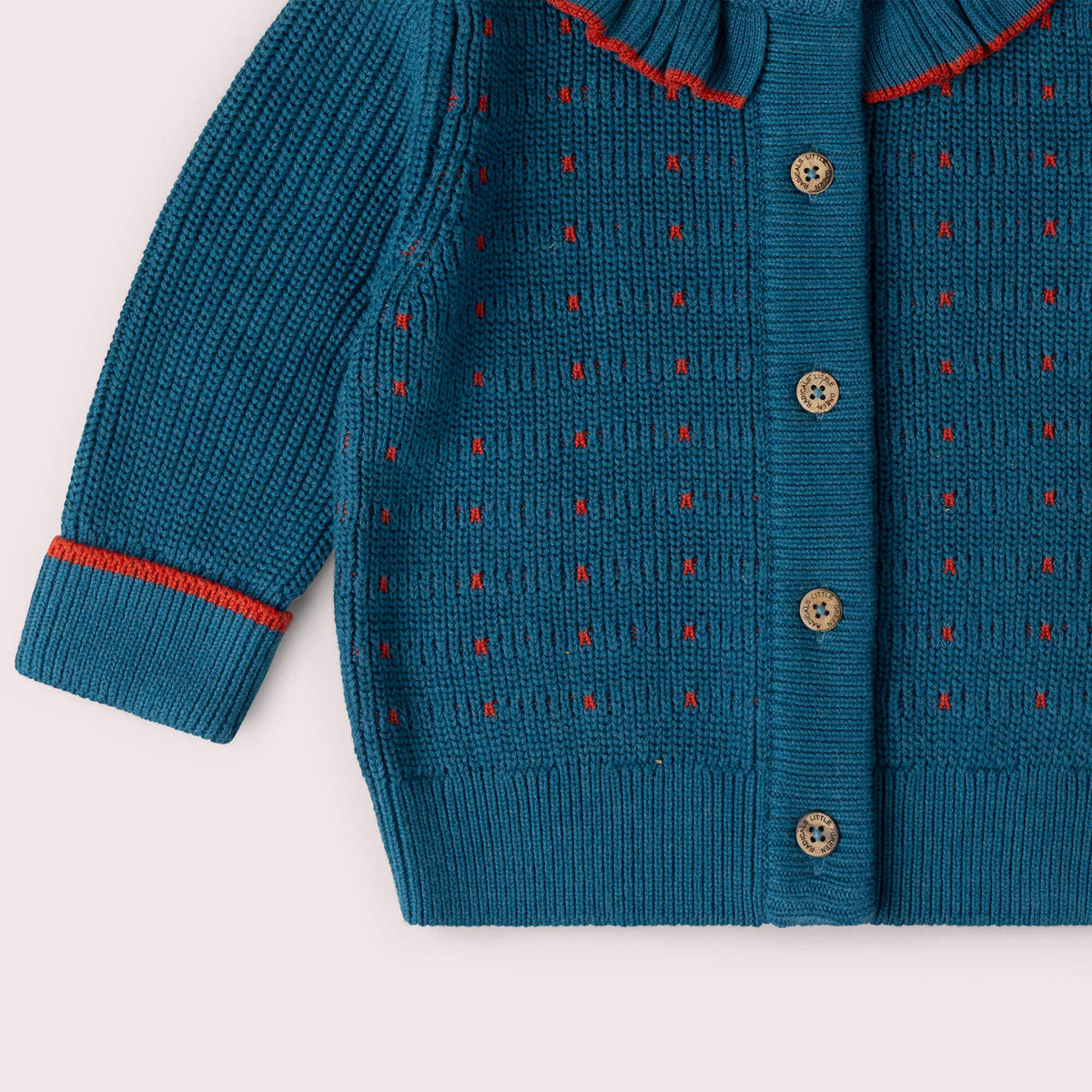 Detail of the buttons, colored stitches and ribbed hem on a teal knitted cardigan.