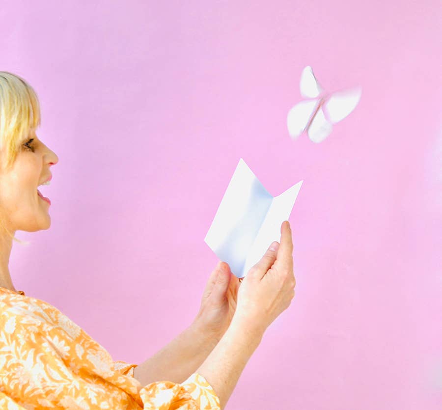 Woman holding a white paper butterfly against a pink background