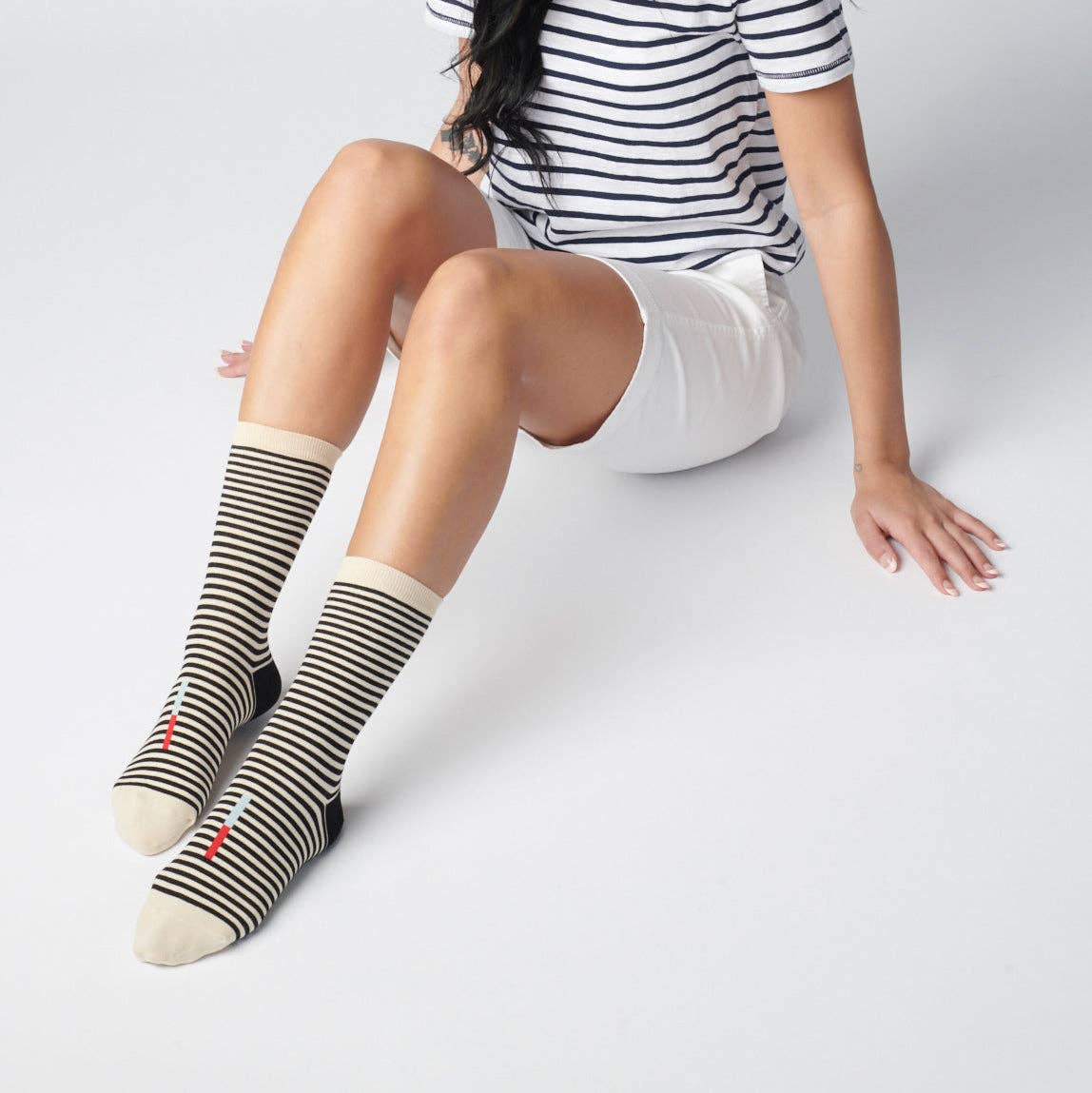 Woman wearing black and white striped crew socks, white shorts and a black and white striped shirt sitting on a white floor