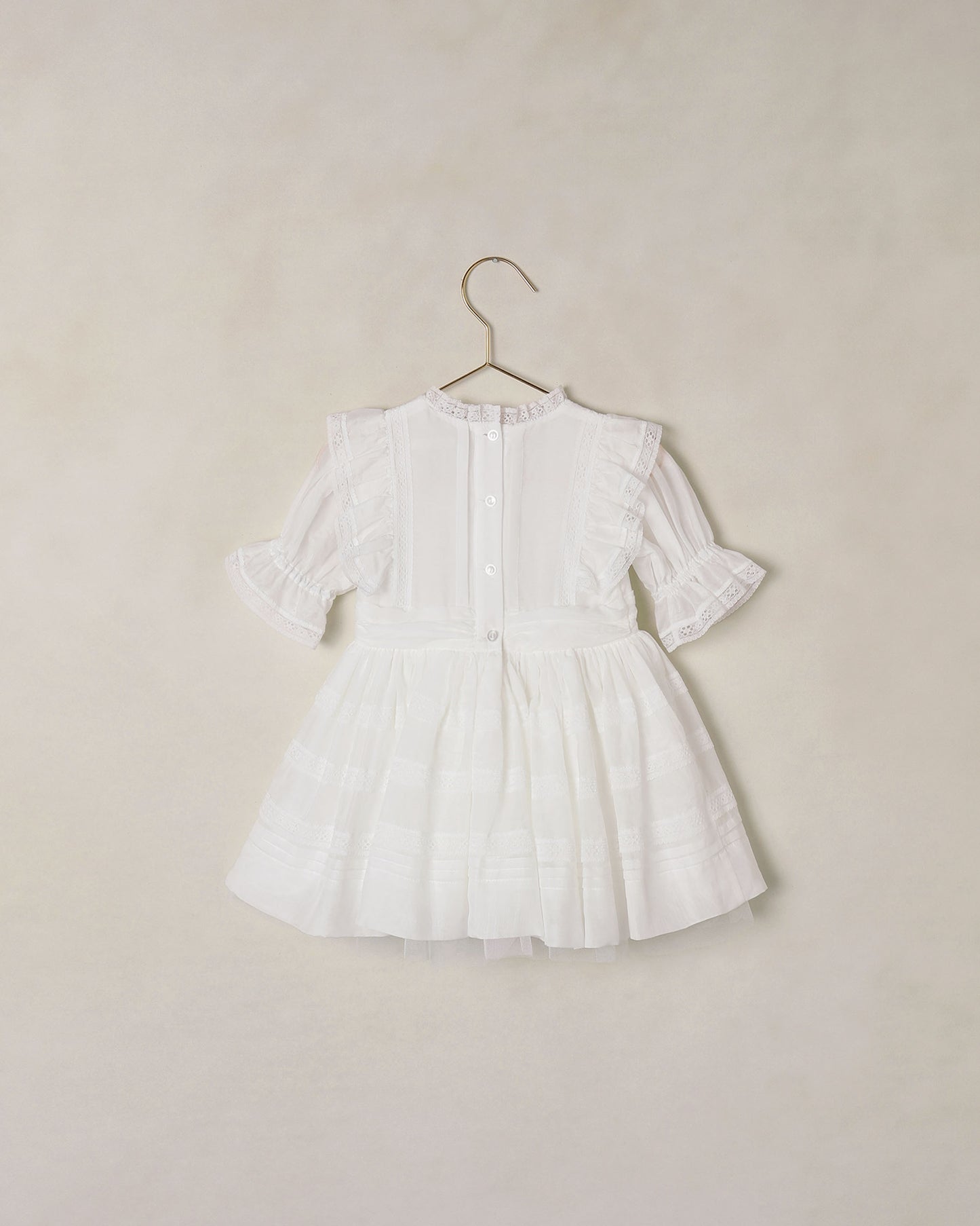 Back of white dress on a hanger against a beige background