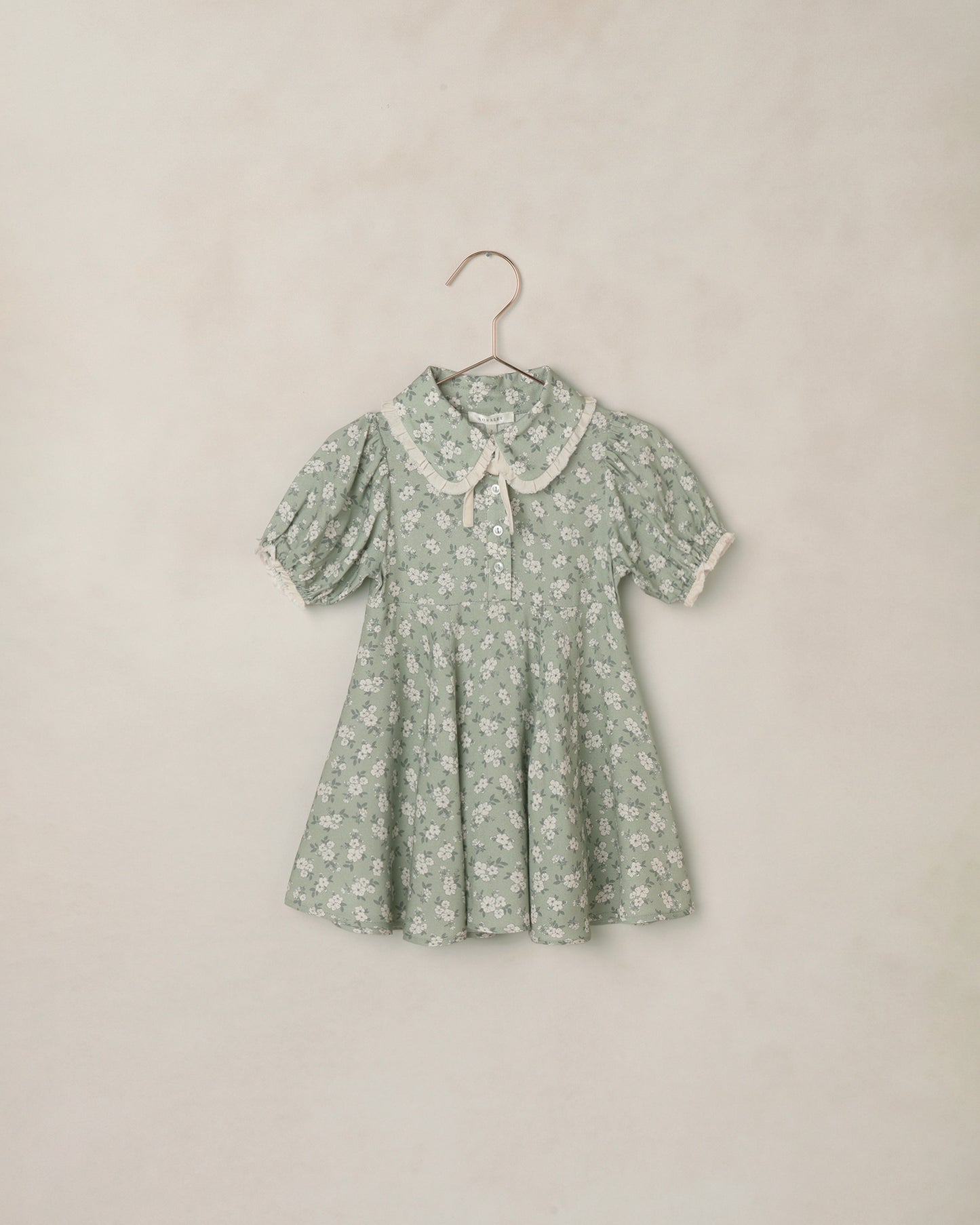 Green floral dress on a hanger against a beige background