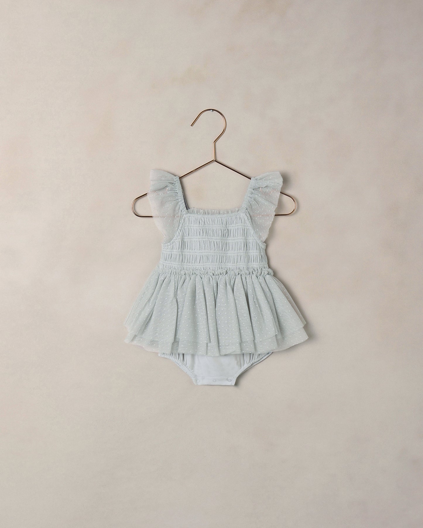Light blue baby romper with ruffled straps on a beige background