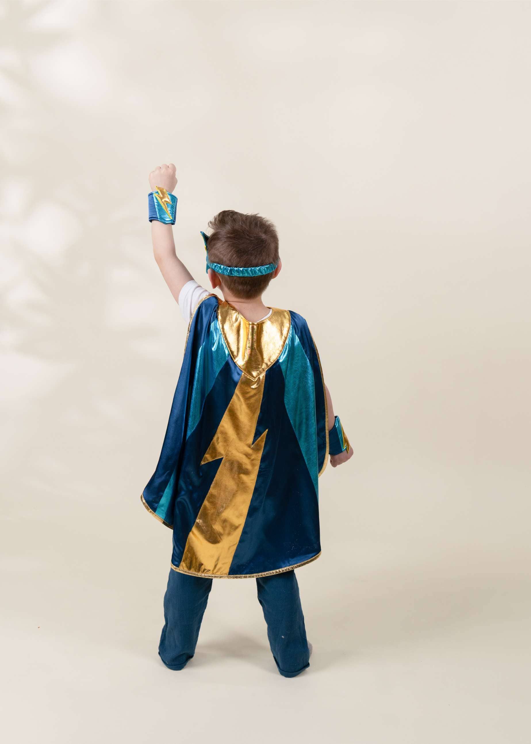 Child wearing a superhero costume with a blue cape and gold accents on a plain background