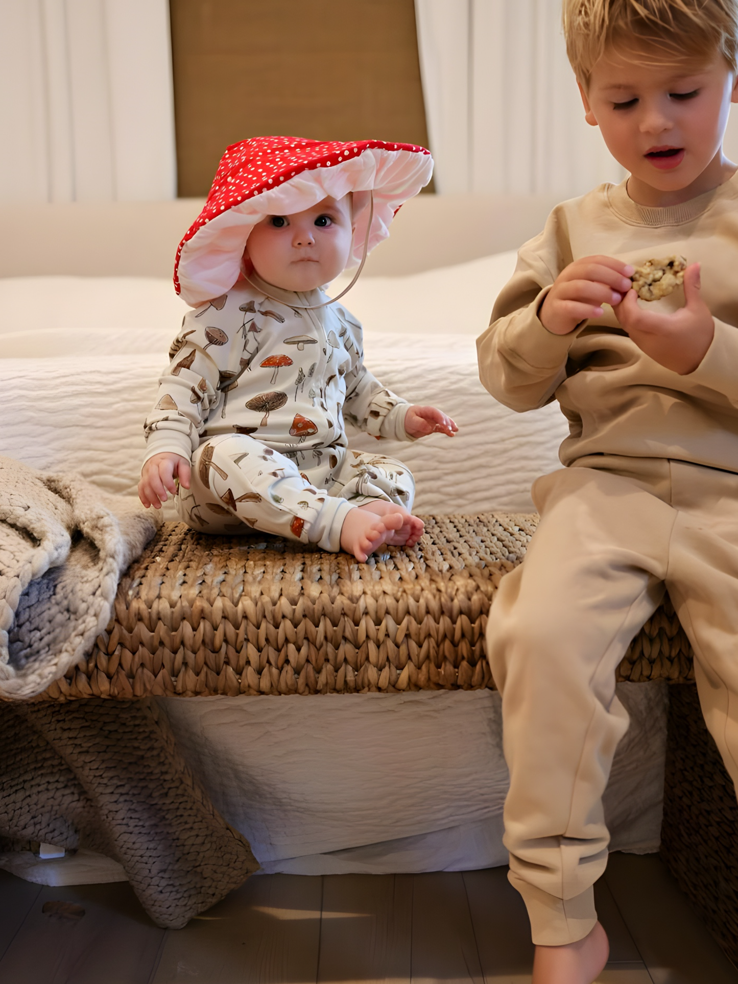 Two children sitting on a woven bench with a neutral background