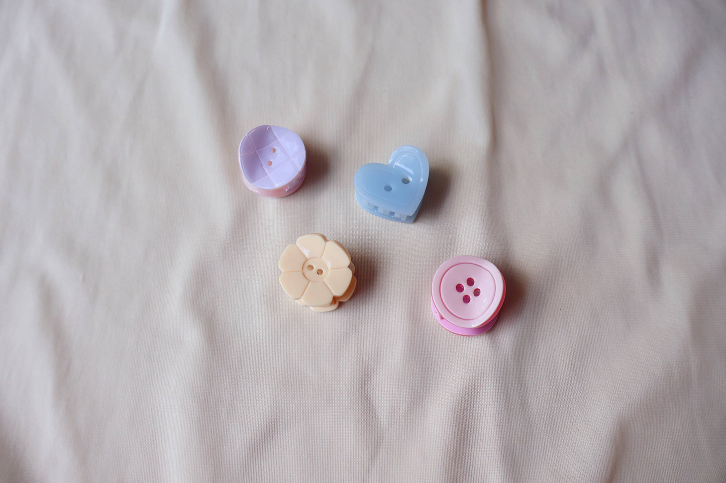 Four colorful button shaped hair clips on a beige fabric background