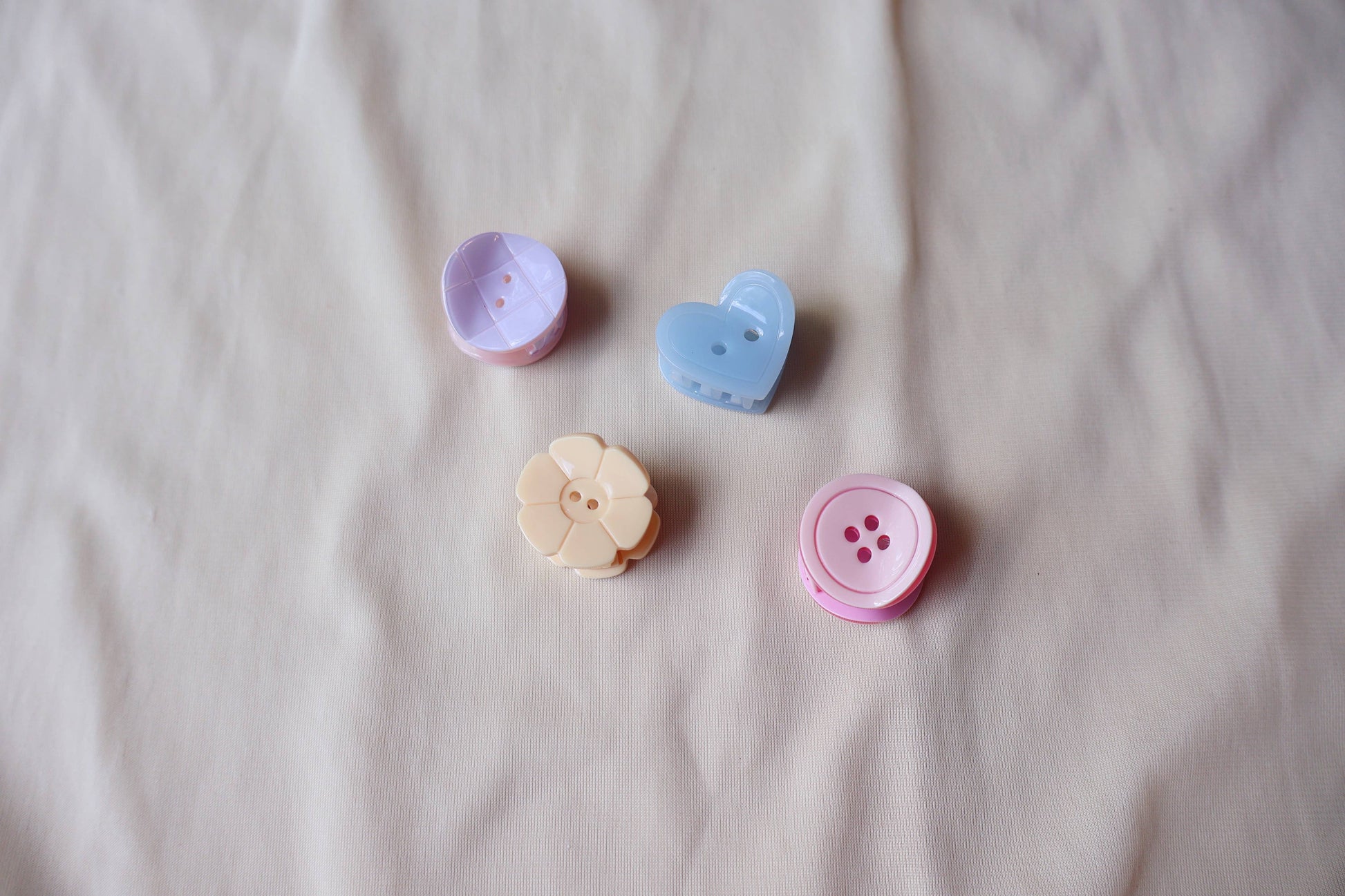 Four colorful button shaped hair clips on a beige fabric background