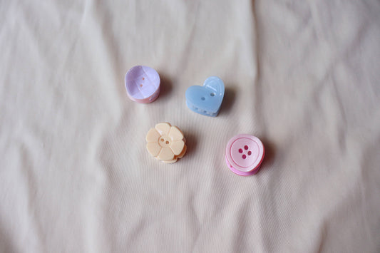 Four colorful button shaped hair clips on a beige fabric background