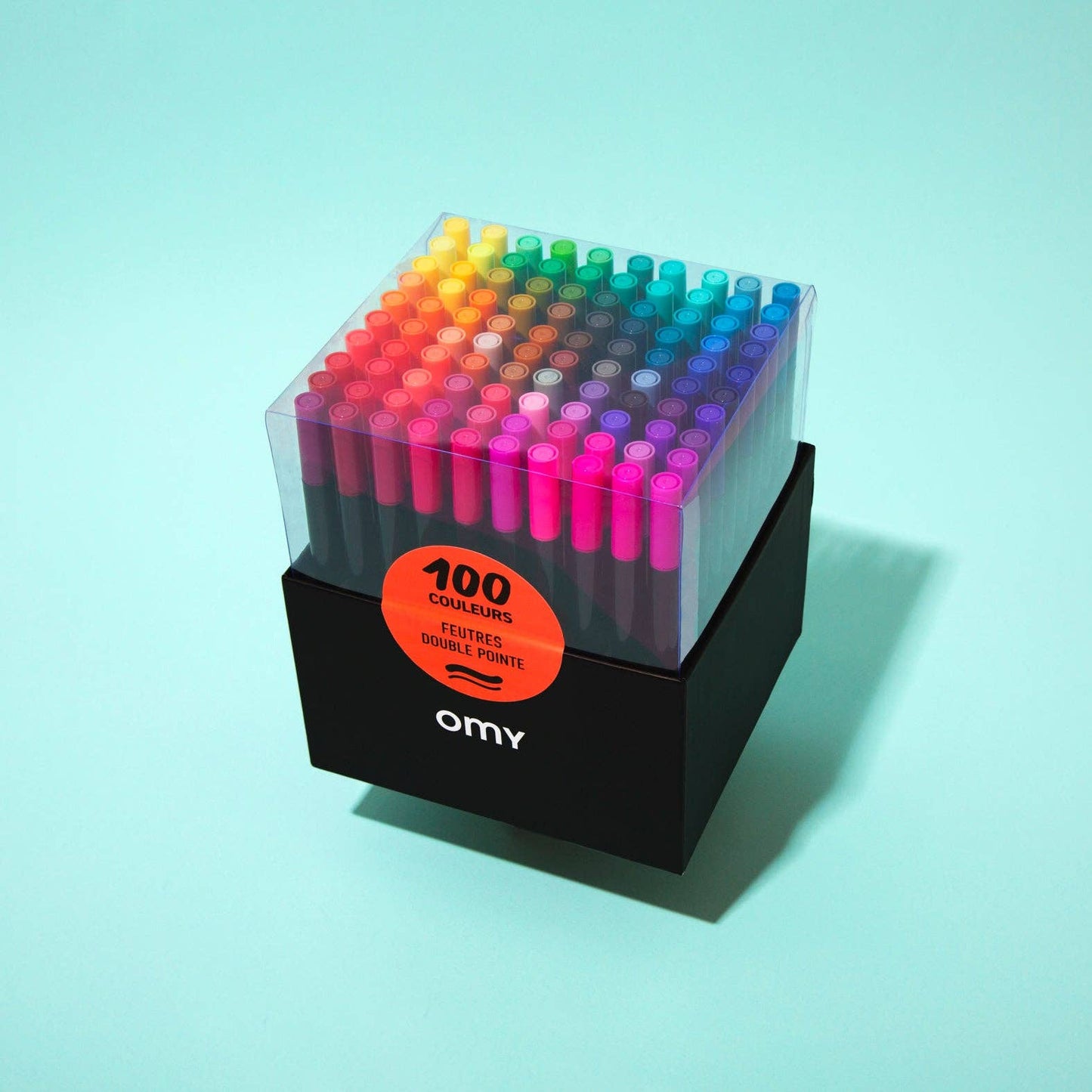 Set of 100 colorful markers in a clear holder with 'omy' branding on a light blue background