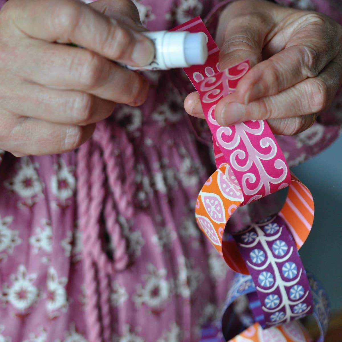 Hands applying glue to a pink patterned paper strip while assembling Paperchain 4.
