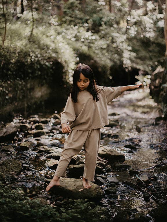 Child in beige outfit standing on rocks in a forest stream