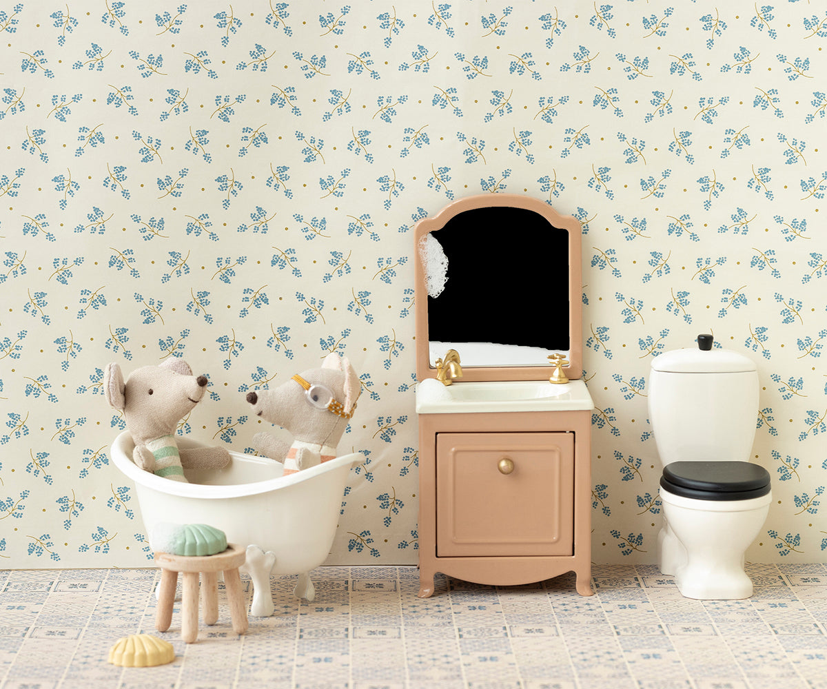 Miniature bathroom setup with a sink, toilet, and bathtub against floral wallpaper.