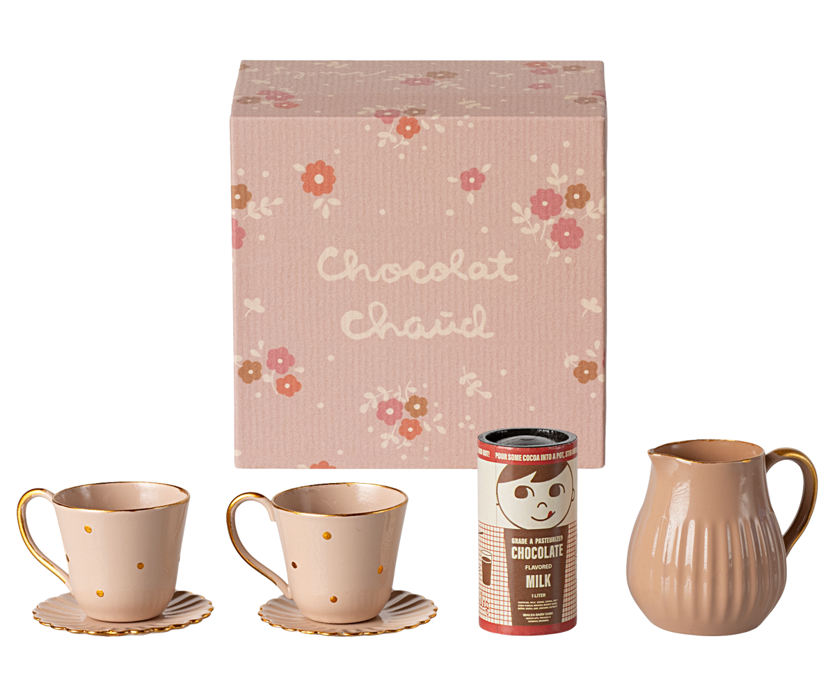 Miniature ceramic mugs, a pitcher, and a can of chocolate milk in front of a floral-patterned box labeled 'Chocolat Chaud'.