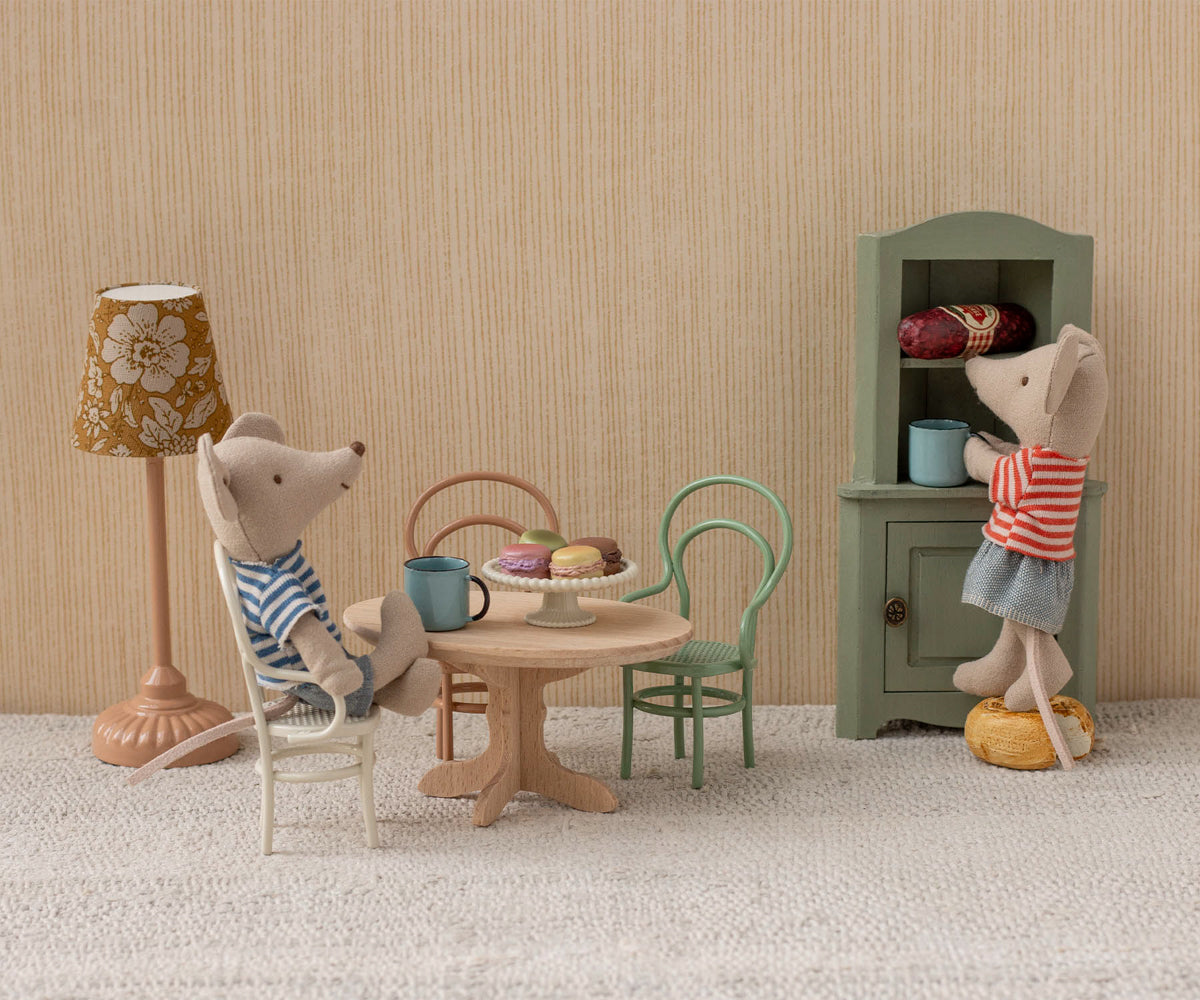 interior dollhouse scene with wooden table, three chairs, a floor lamp, and a cabinet with two maileg mice