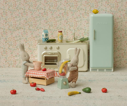 Miniature kitchen scene with toy refrigerator, oven, and rabbits in a room with floral wallpaper.