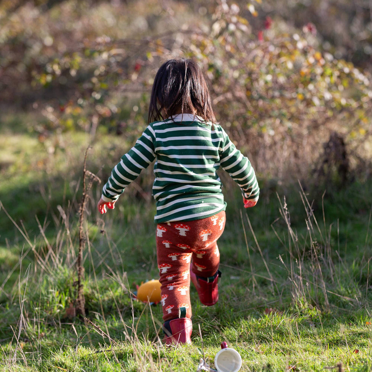 Rear view of a child wearing rust mushroom joggers and a green striped top outdoors.
