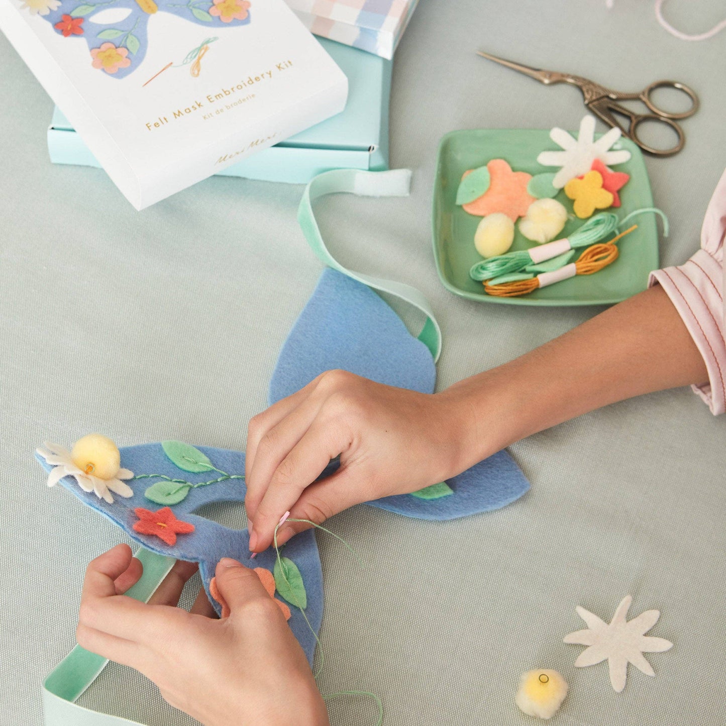 Hands working on a craft project with felt materials and tools on a table.