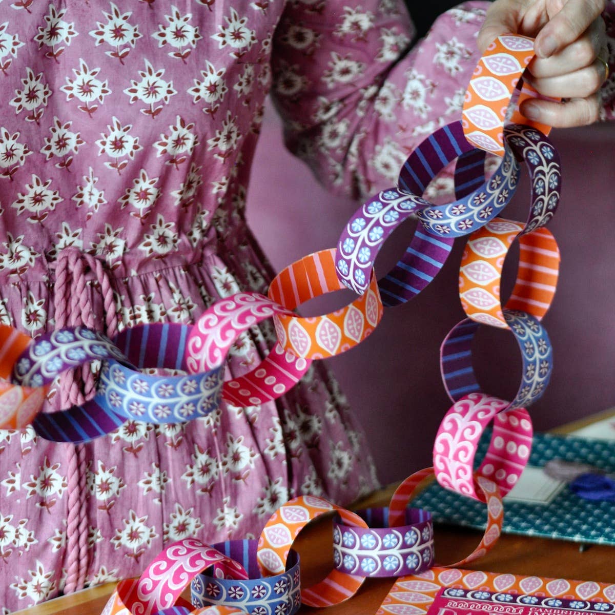 Person holding up assembled pink, orange, blue and purple patterned paper chains.