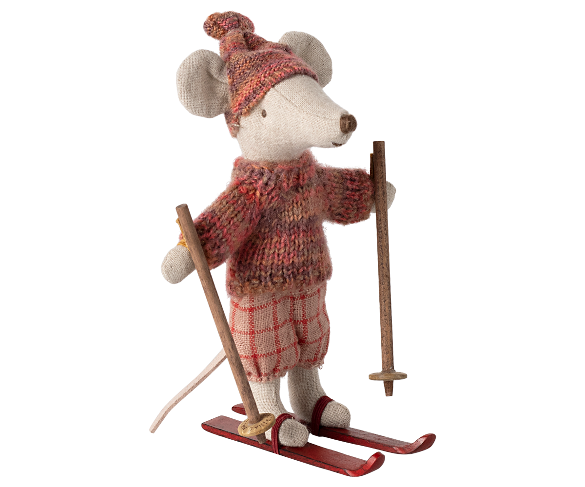 A plush mouse figurine dressed in winter clothing, including a knit hat, sweater, and plaid skirt, holding ski poles and standing on red skis against a plain white background.