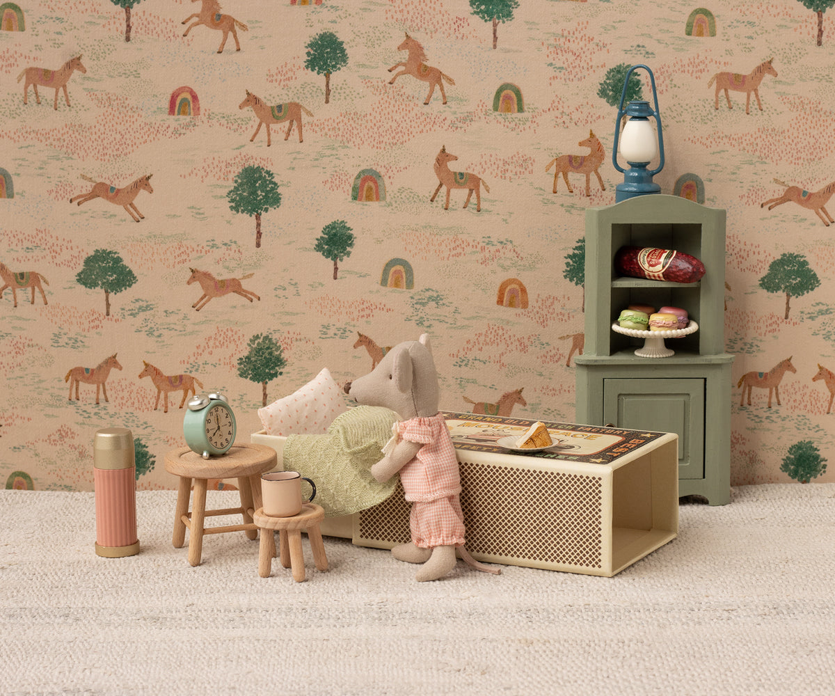 Miniature dollhouse scene with a girl, furniture, and decorative items against a wallpaper with horse pattern.