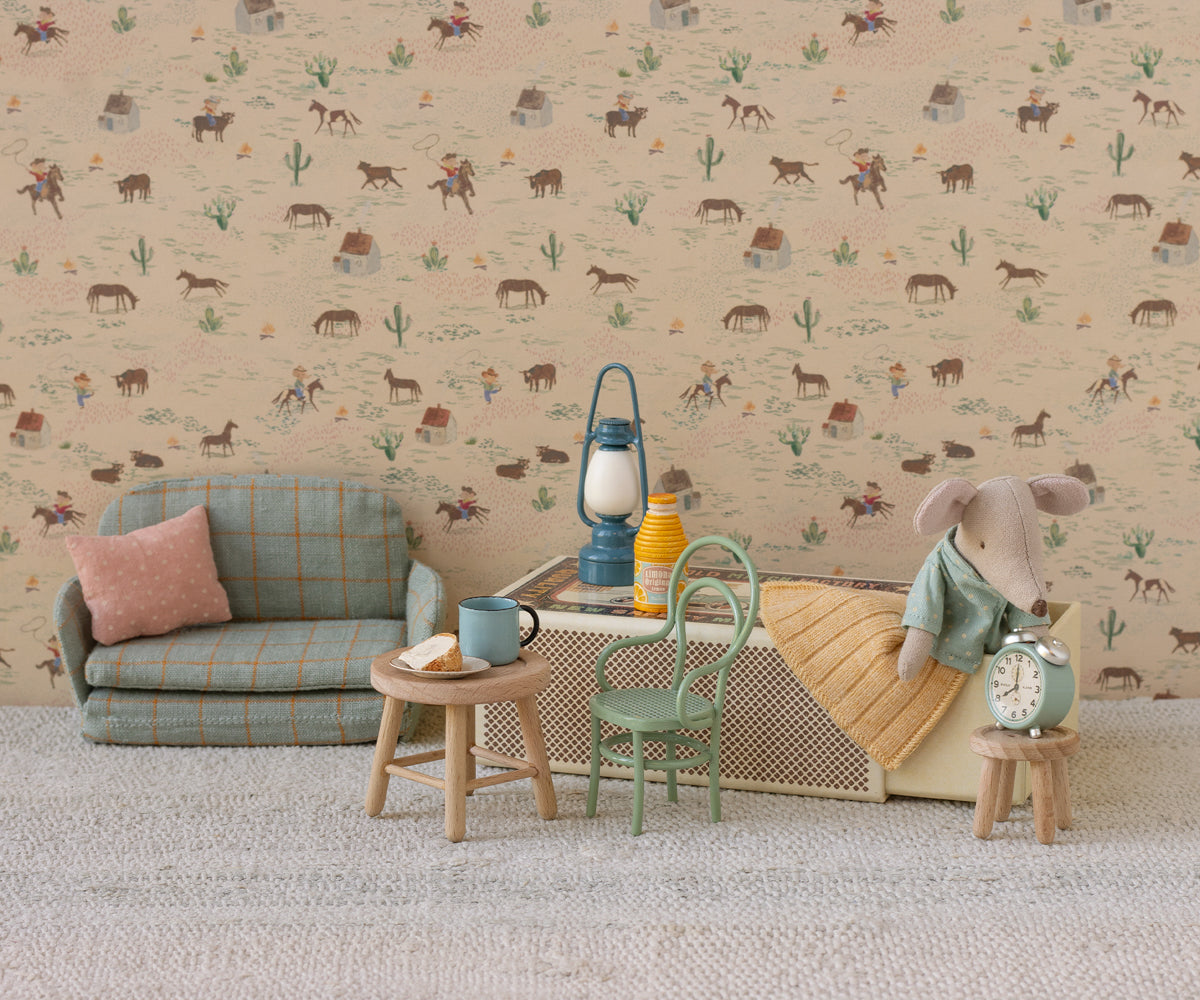 Dollhouse room with patterned wallpaper, sofa, and small table featuring toy mouse in a matchbox bed.