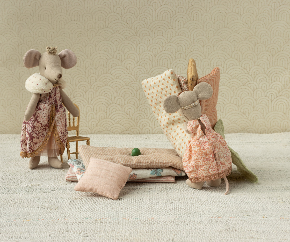 Two plush mouse toys with decorative clothing on a textured surface with a patterned wall background.