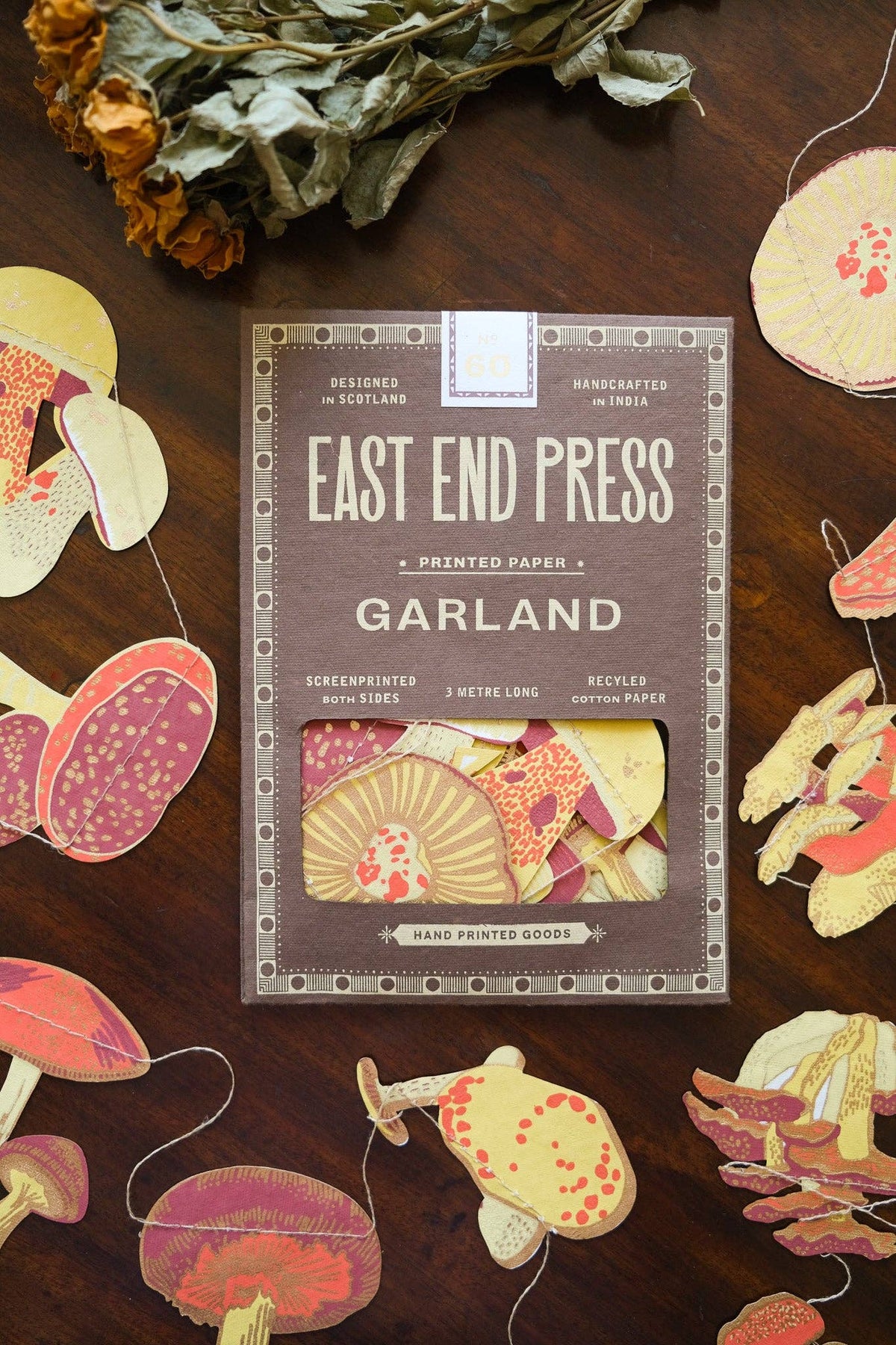 East End Press Mushroom Sewn Garland box surrounded by mushroom cutouts and dried flowers on dark wood.