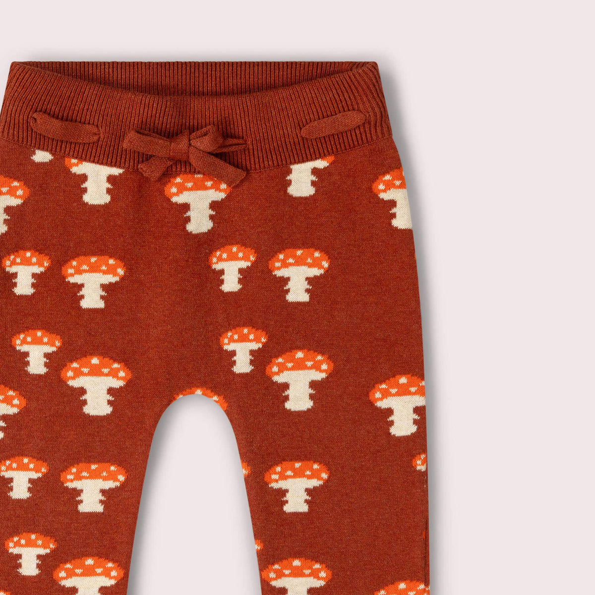 Detail of the tied drawstring waistband and mushroom pattern on rust knitted joggers.