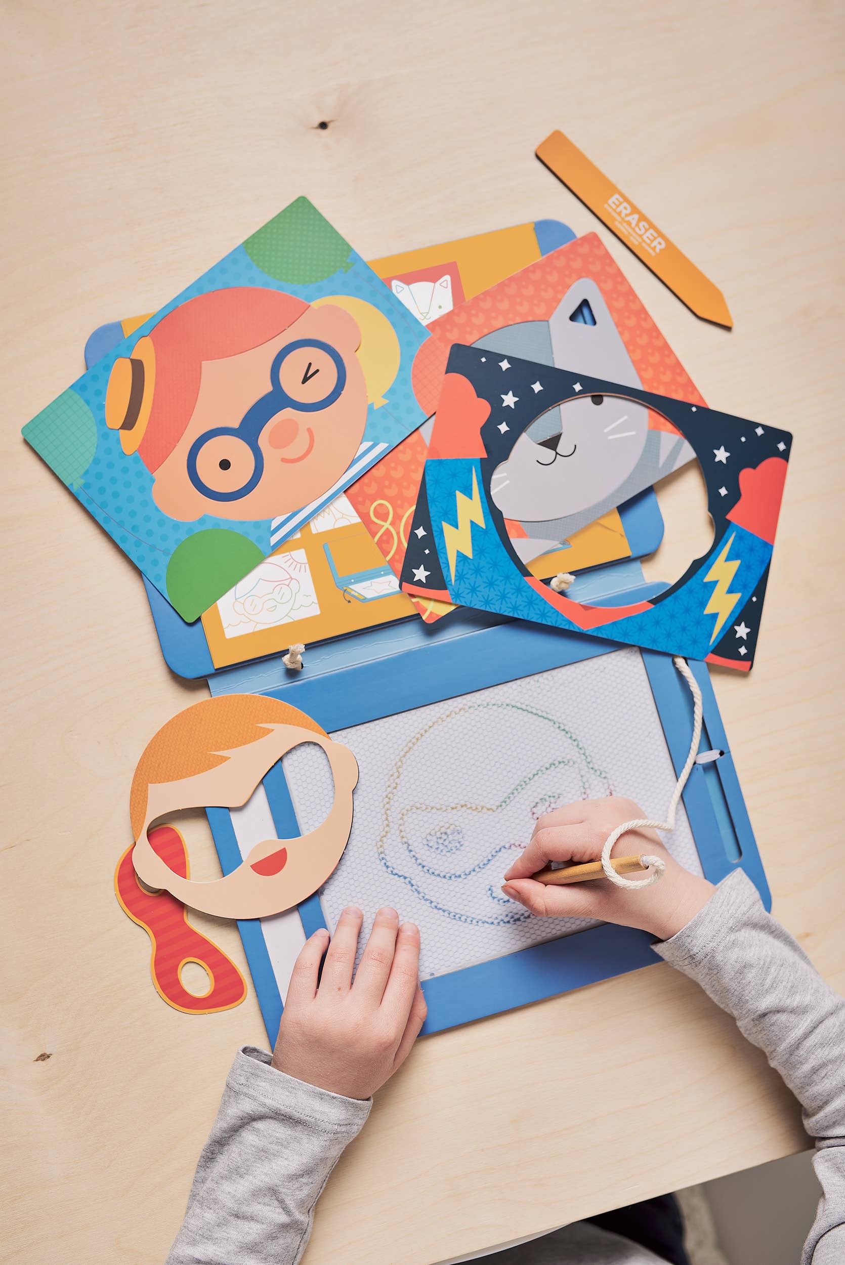 Child's hands using a drawing tool on magnetic sketchboard with face stencils