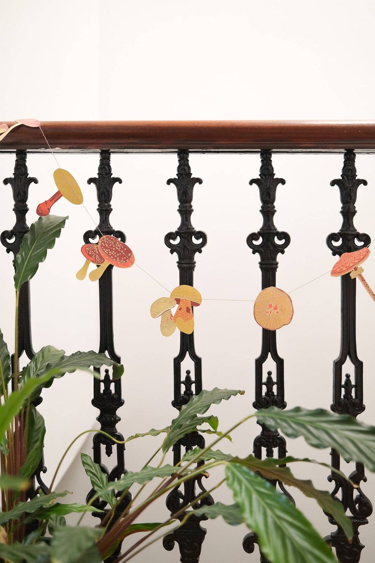 Yellow and red mushroom paper garland draped across a black metal stair railing above green plants.