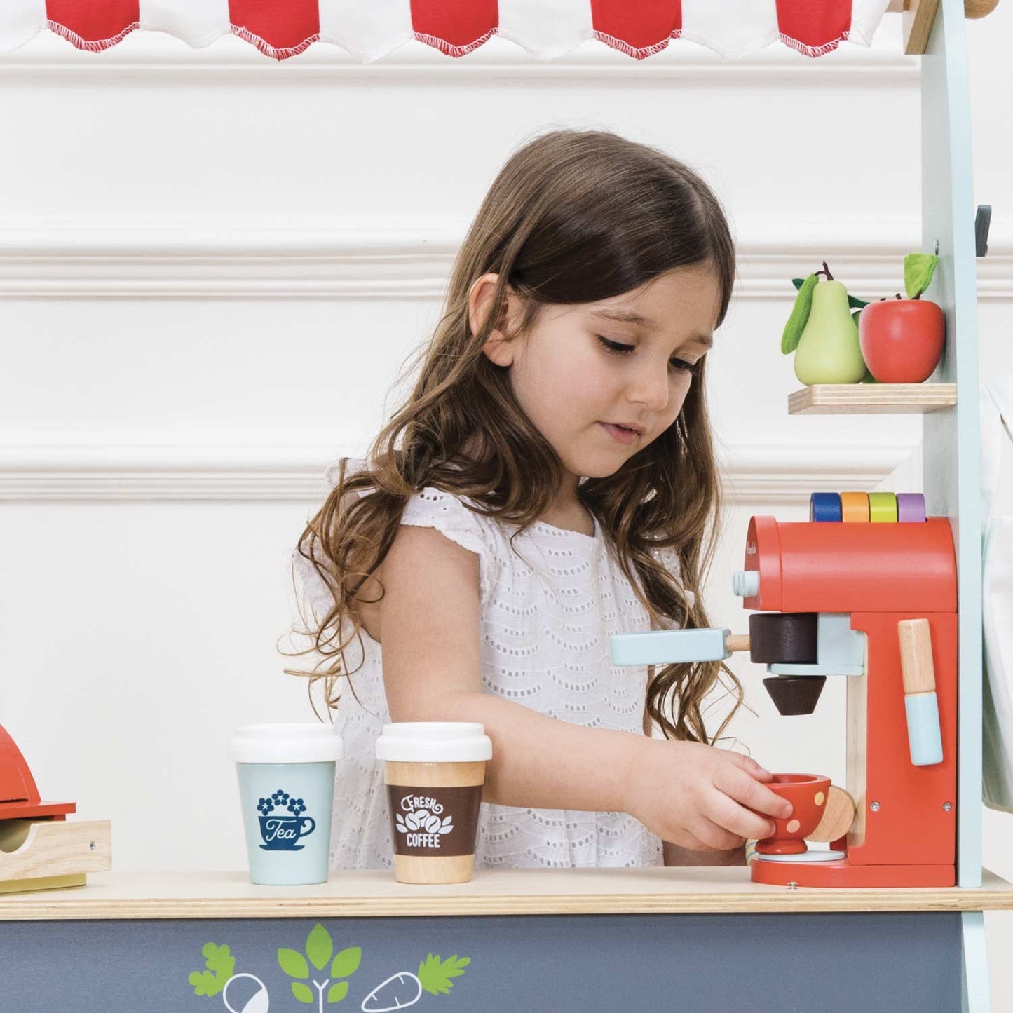 Young girl playing with a toy coffee machine in a kitchen setting