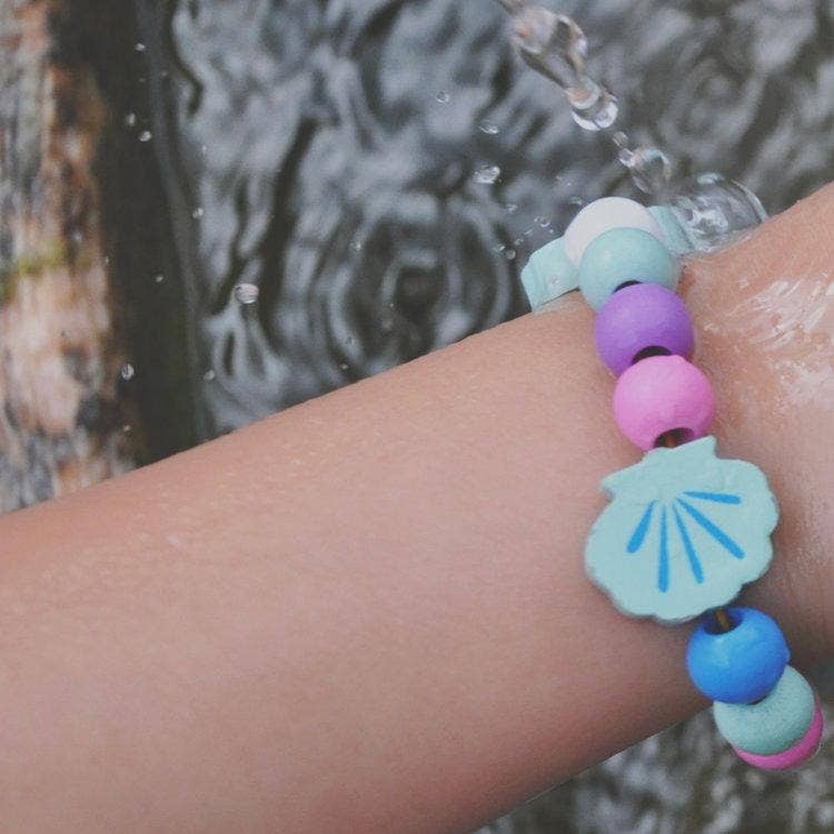 Colorful beaded bracelet with a shell charm on a wrist against a water background